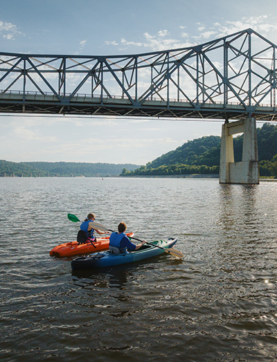 two kayakers on a river with a bridge in the background